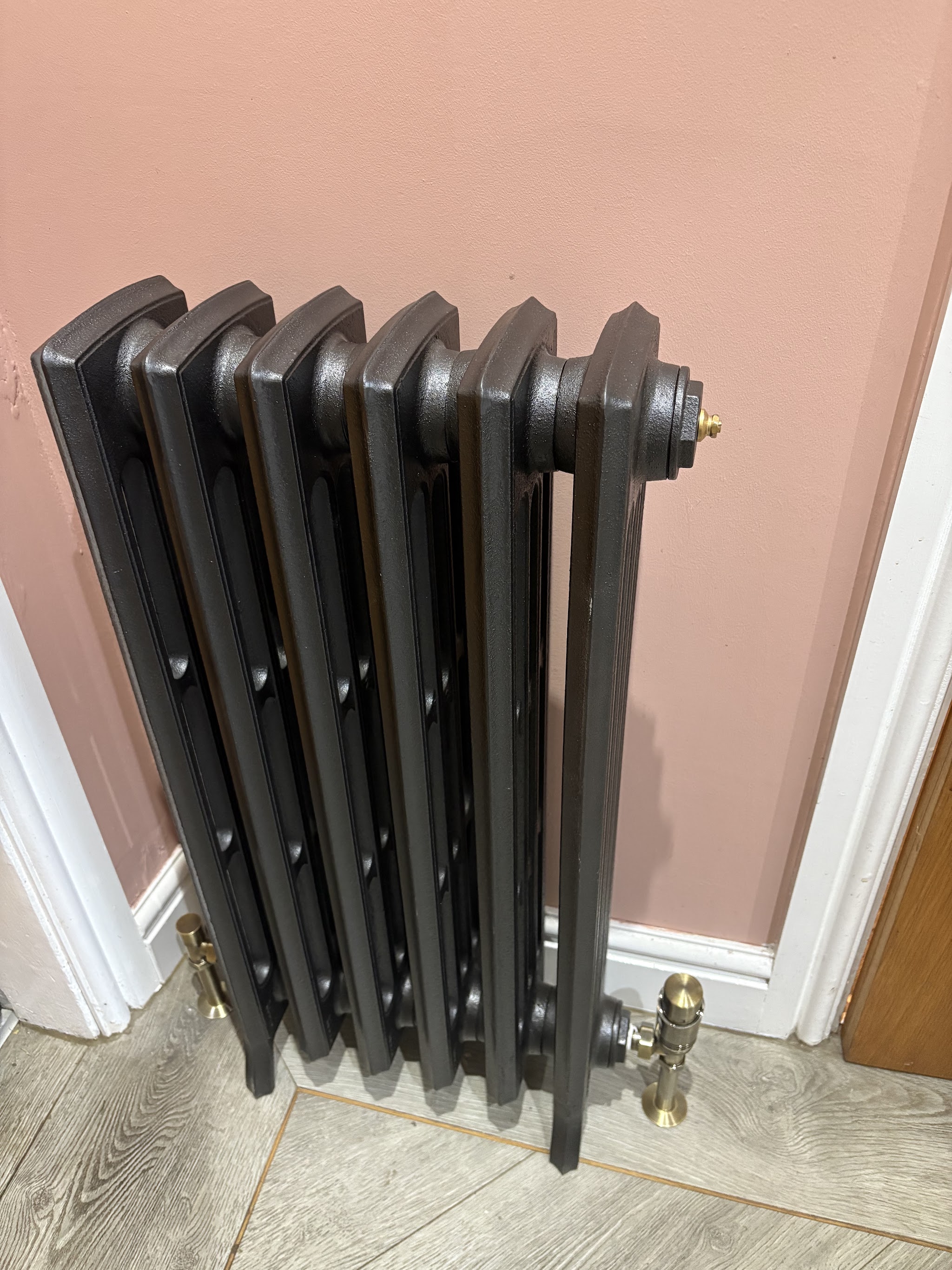 Dark column radiator fitted beside a doorway, with neat floor-level pipework